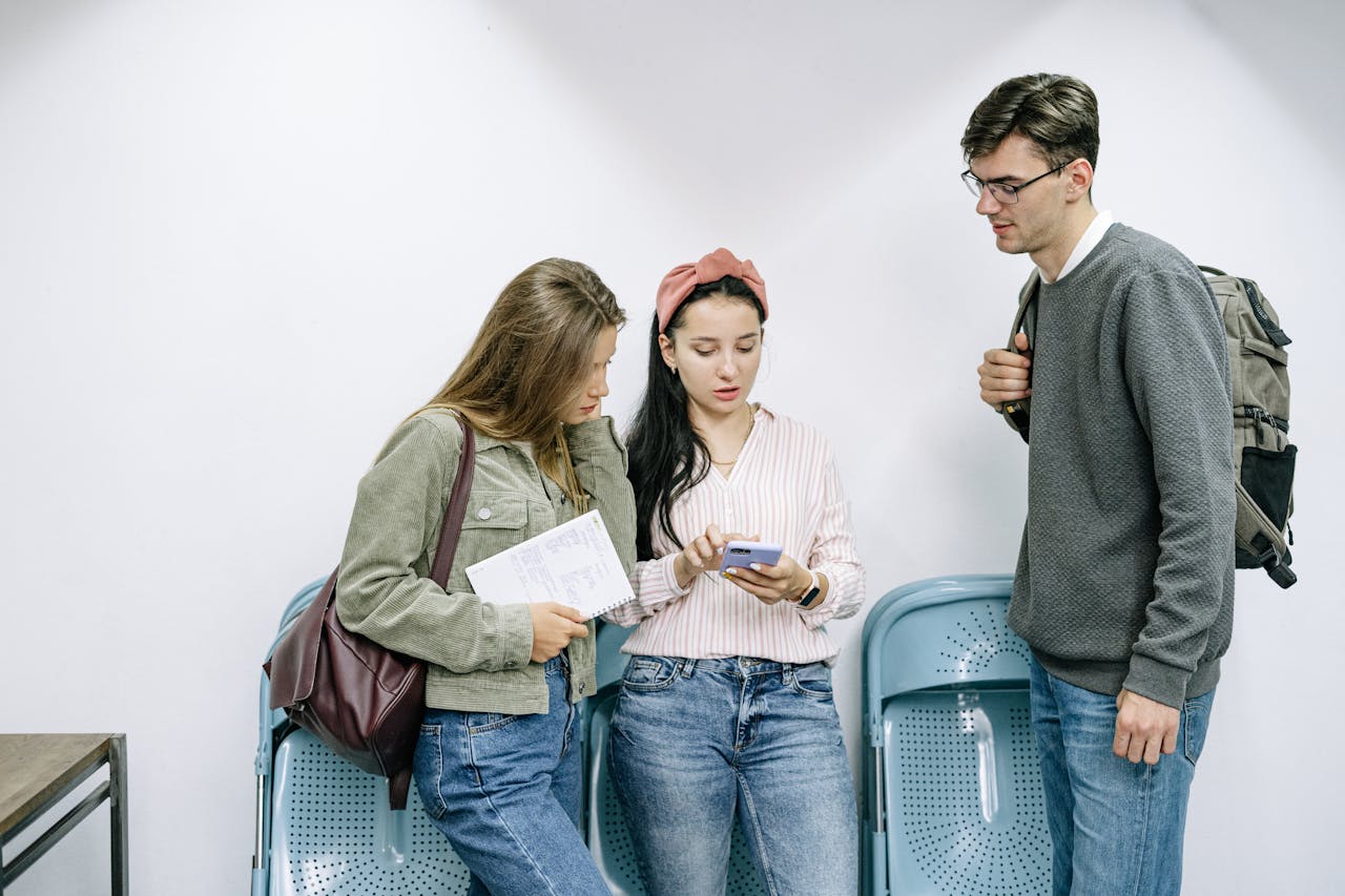 Three young adults stand together using a smartphone indoors.